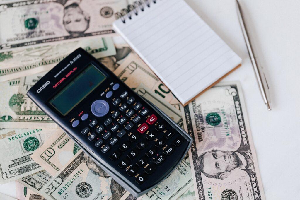 calculator and notepad placed on US dollar stack