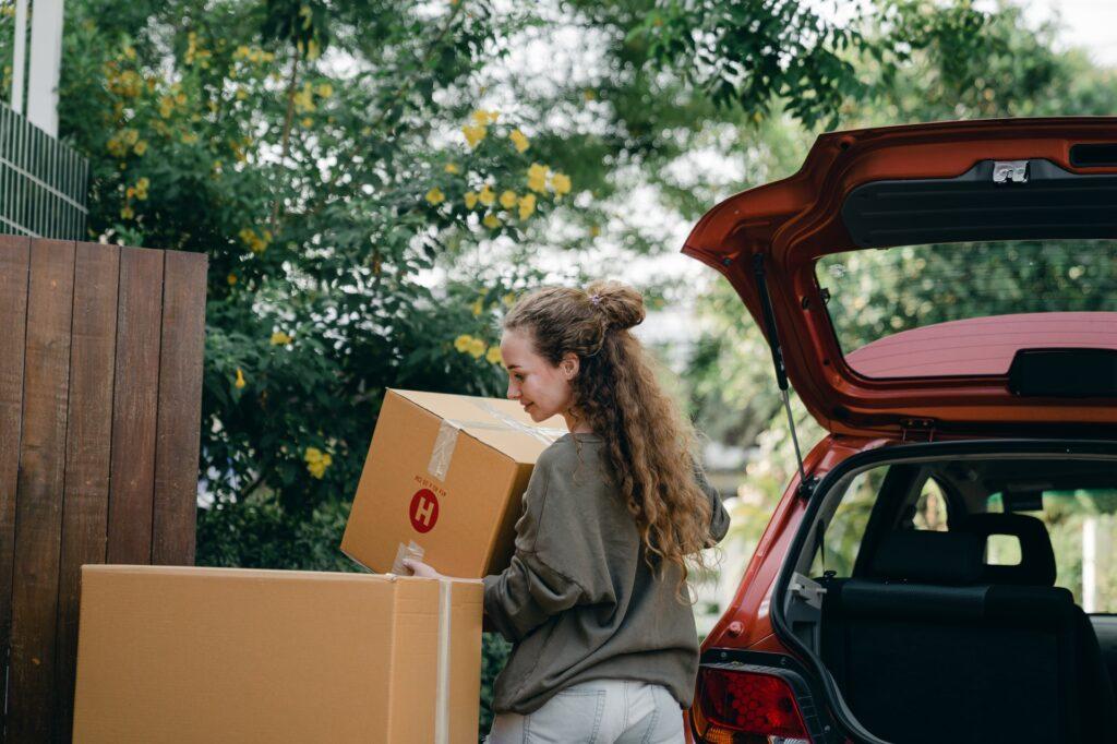 young woman carrying box to new home while unpacking car